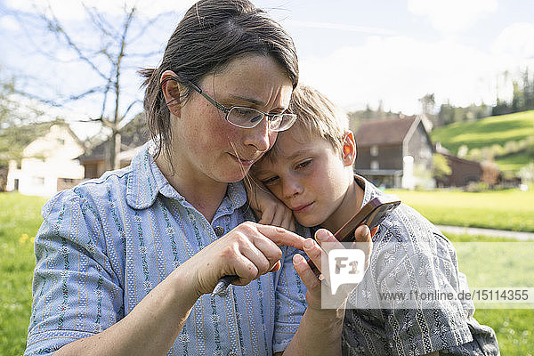 Mutter mit Sohn benutzt tragbares Gerät im Freien