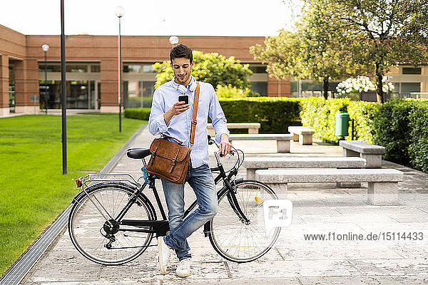 Young man with bicycle using smartphone  headphones around neck in the city