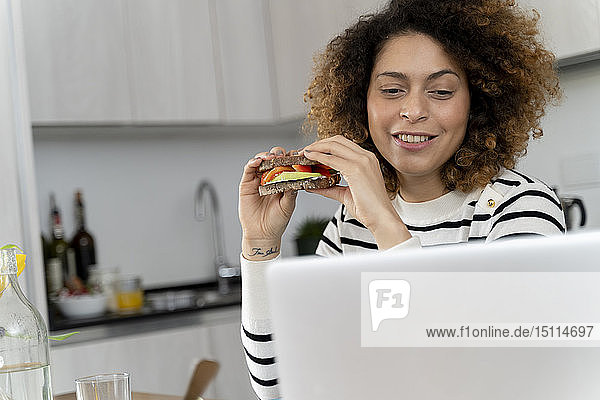 Woman using laptop while eating a sandwich