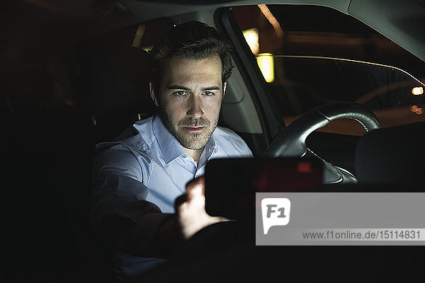 Young man using cell phone in car at night