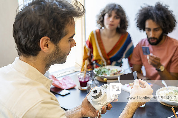Freunde beim Mittagessen in einem Restaurant beim Betrachten von Sofortbildern