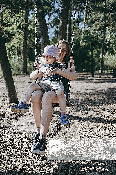 Happy mother with little daughter on swing on a playground