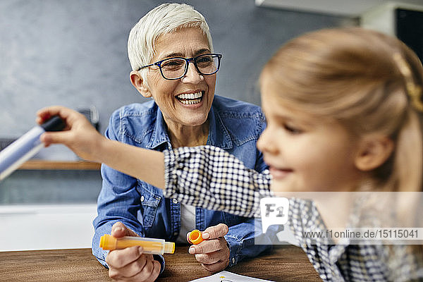 Großmutter und Enkelin sitzen am Tisch und malen ein Malbuch
