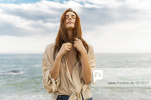 Porträt einer rothaarigen jungen Frau mit Nasenpiercing vor dem Meer stehend