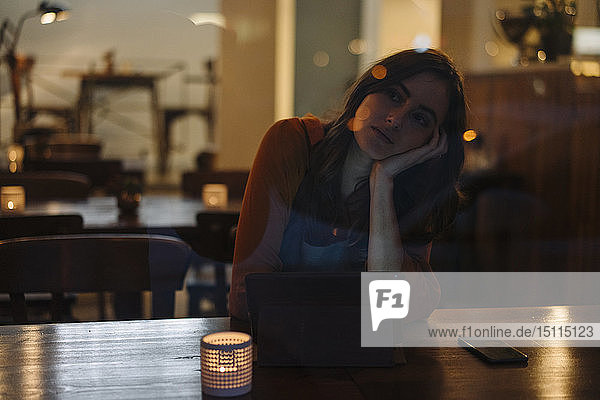 Serious young woman sitting at table in a restaurant using tablet