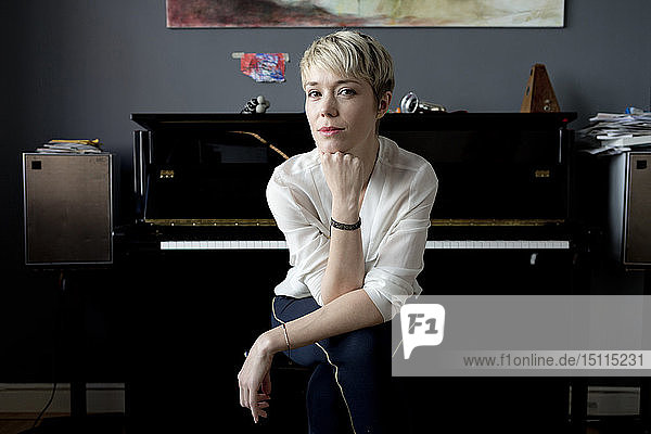 Porträt einer blonden Frau  die in ihrem Musikzimmer vor dem Klavier sitzt
