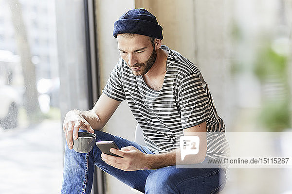 Young man holding coffee cup using cell phone