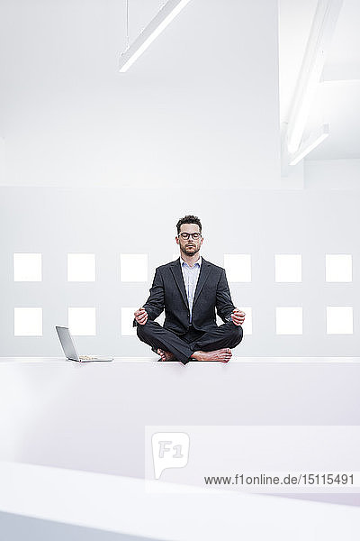 Geschäftsmann macht Yoga im Büro neben dem Laptop