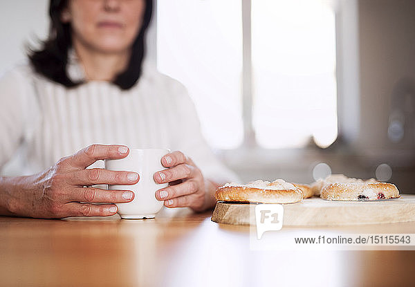 Reife Frau sitzt am Küchentisch und trinkt Kaffee