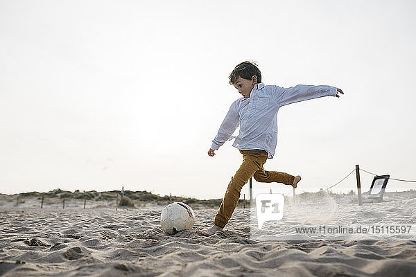 Kleiner Junge spielt am Strand Fussball und kickt den Ball