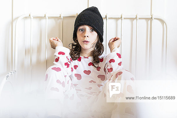 Porträt eines kleinen Mädchens  das mit Mütze und Pyjama im Bett sitzt