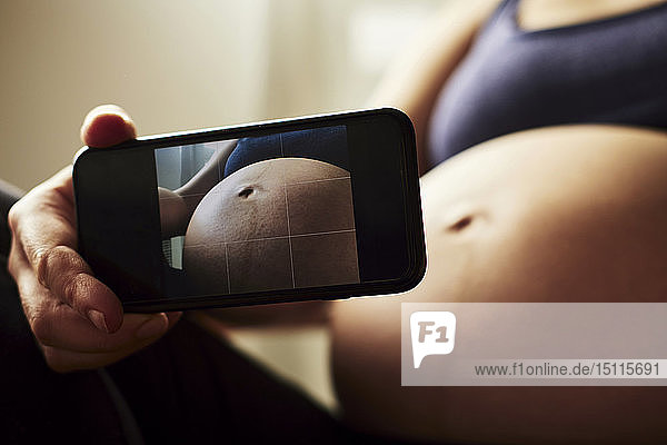 Schwangere Frau macht ein Foto von ihrem Babybauch