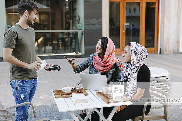 Junge Frau bezahlt bargeldlos mit Smartphone in einem Café