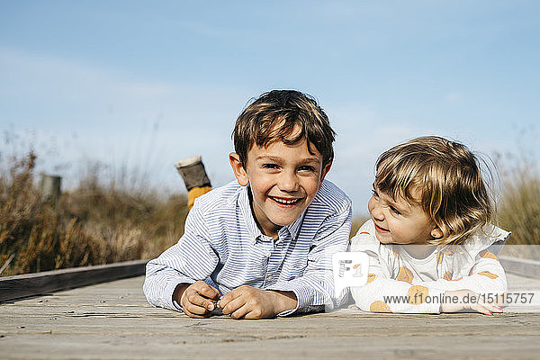 Porträt eines Jungen und seiner kleinen Schwester  die Seite an Seite auf einer Strandpromenade liegen und sich amüsieren