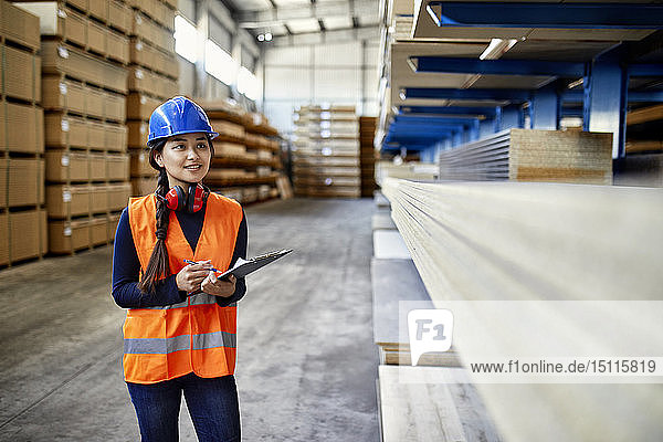 Smiling female worker with clipboard in factory warehouse