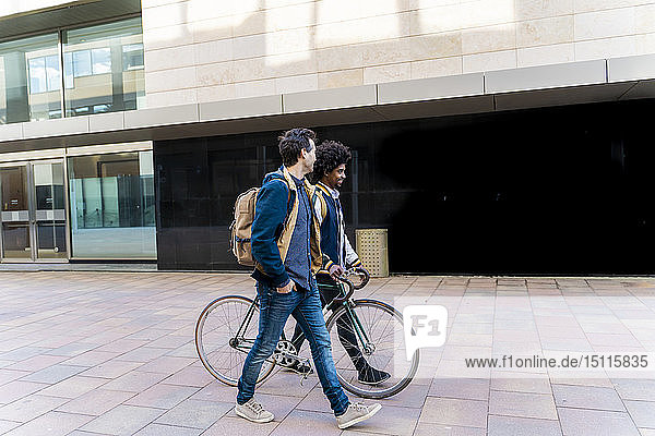 Two casual businessmen with bicycle walking in the city  Barcelona  Spain
