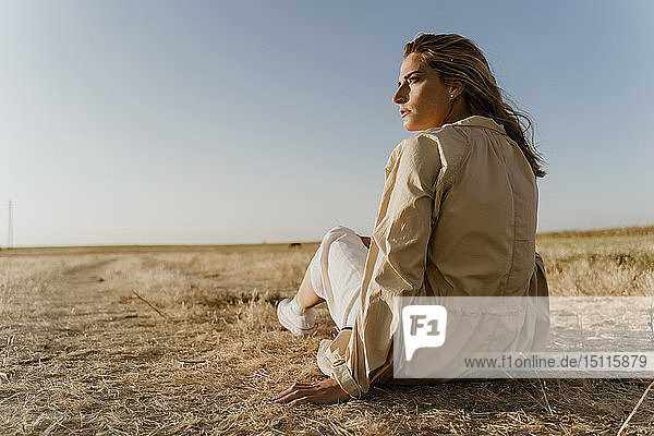 Female traveller sitting on dry meadow  looking sideways
