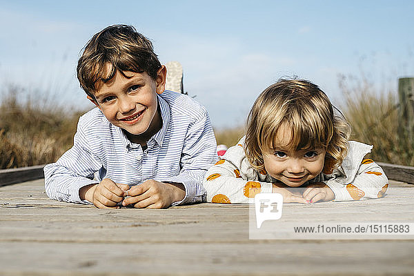 Porträt eines lächelnden Jungen und seiner kleinen Schwester nebeneinander liegend auf der Promenade