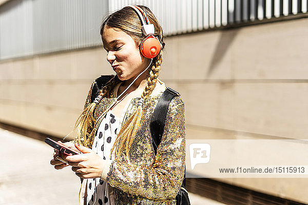 Smiling girl wearing golden sequin jacket and headphones looking at cell phone