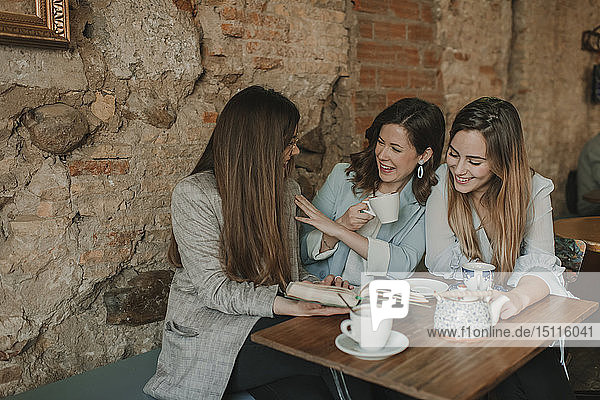 Three happy young women having fun reading a book in a cafe