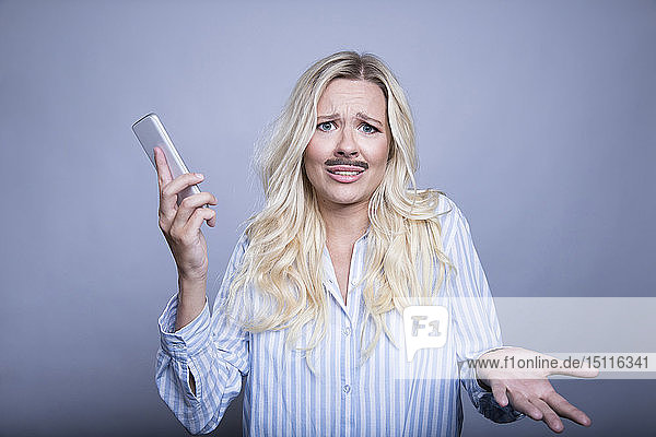 Porträt einer fragenden blonden Frau mit falschem Schnurrbart und Smartphone