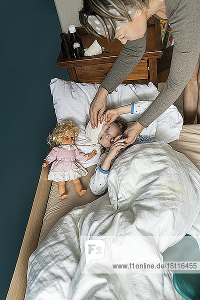 Mutter nimmt Temperatur einer kranken  im Bett liegenden Tochter