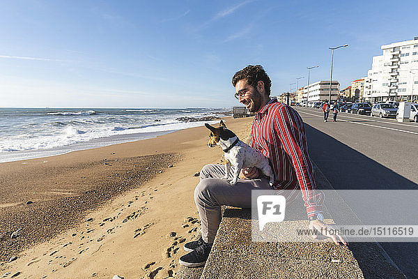 Portugal  Porto  glücklicher junger Mann sitzt mit seinem Hund auf dem Schoß am Strand