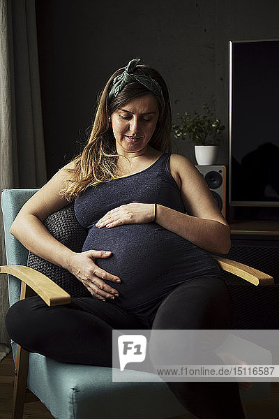 Schwangere  die zu Hause auf ihren Babybauch schaut
