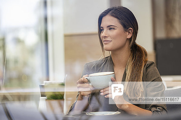 Junge Geschäftsfrau mit Kaffeetasse in einem Café  durch ein Fenster gesehen