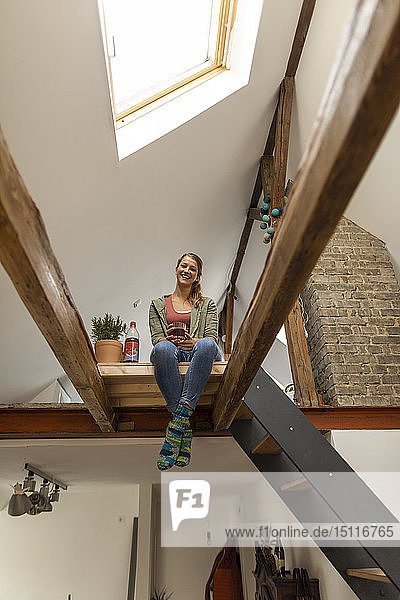 Lächelnde junge Frau sitzt auf dem Dachboden