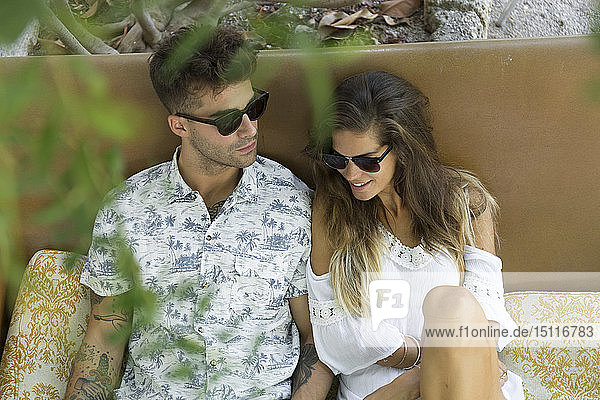 Entspanntes junges Paar mit Sonnenbrille sitzt im Freien