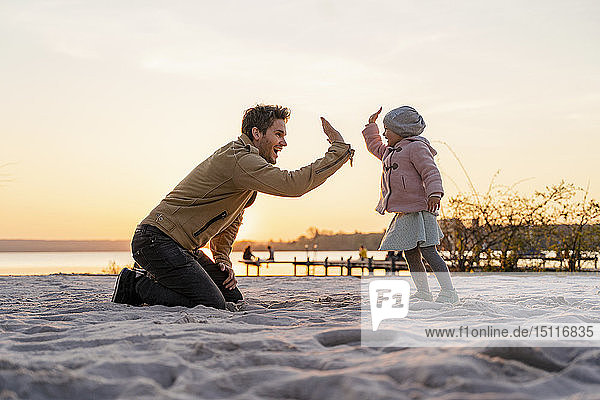 Deutschland  Bayern  Herrsching  Vater und Tochter spielen bei Sonnenuntergang am Strand