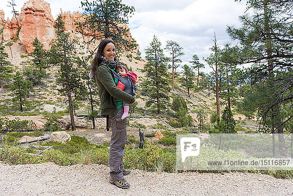 Frau trägt ihre Tochter in einem Tragesitz bei Hoodoos in Bryce Canyon  Utah  USA