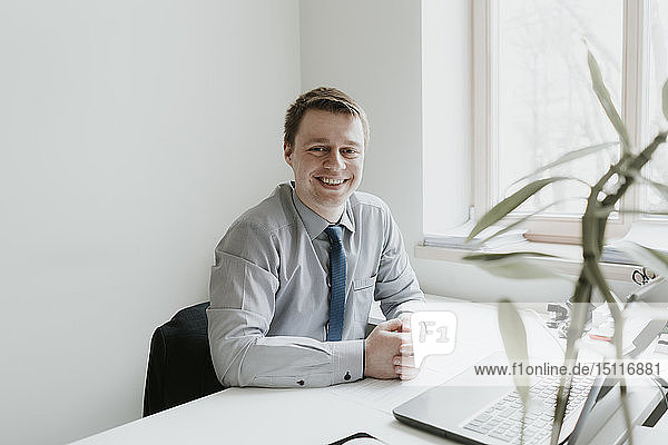 Porträt eines lächelnden jungen Geschäftsmannes  der im Büro am Schreibtisch sitzt