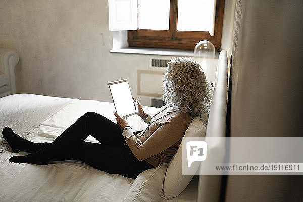 Reife Geschäftsfrau sitzt auf dem Bett und schaut auf das digitale Tablet