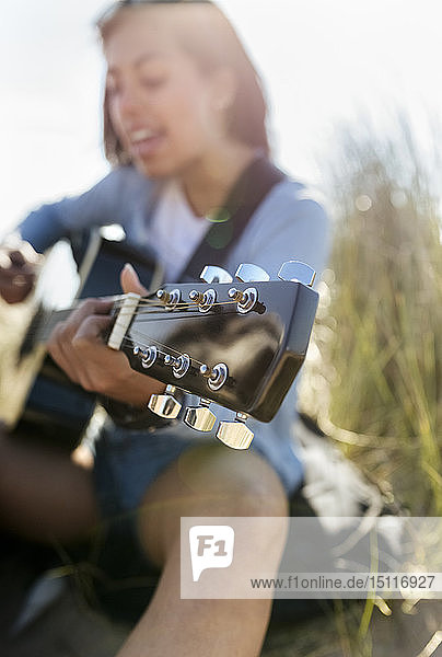 Nahaufnahme einer jungen Frau  die am Strand singt und Gitarre spielt