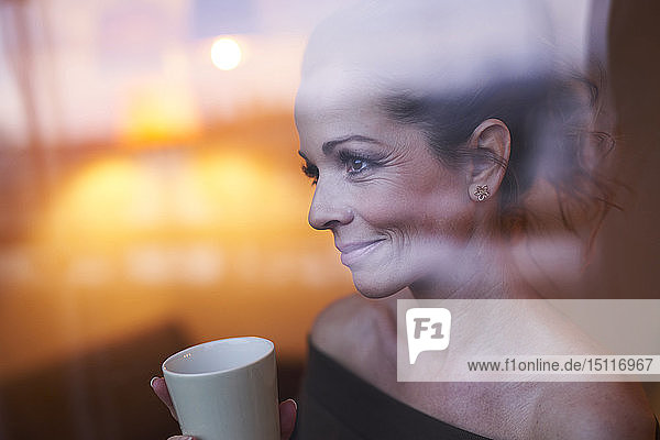 Porträt einer brünetten Frau mit Tasse hinter der Fensterscheibe mit Blick weg