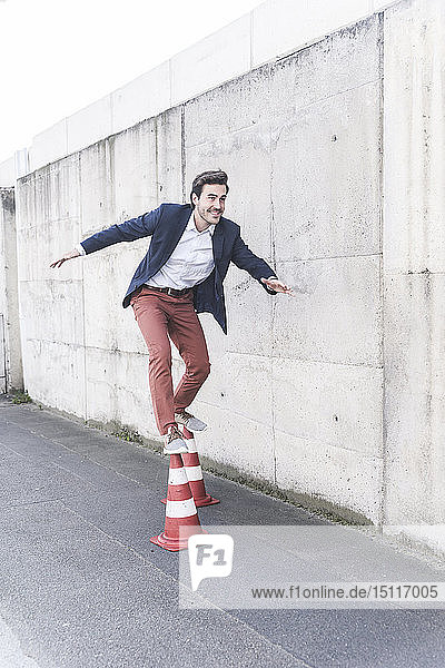 Young man balancing on traffic cones in front of concrete wall