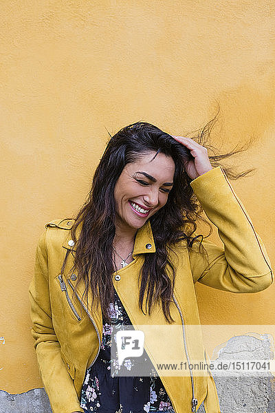 Porträt einer jungen lachenden Frau in gelber Lederjacke  Hand im Haar