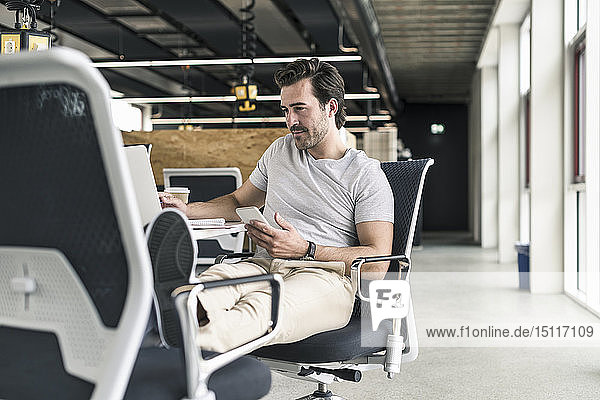 Young businessman working relaxed in modern office  using smartphone and laptop