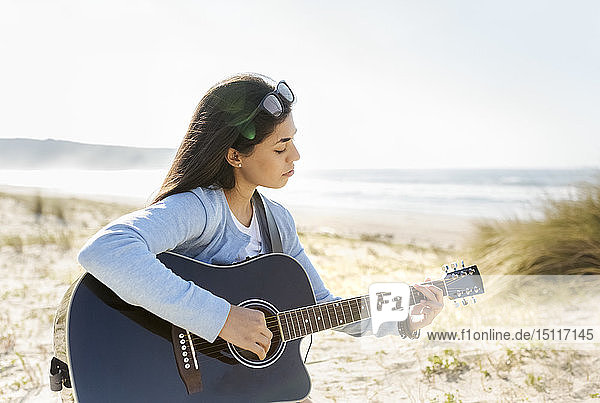 Junge Frau spielt Gitarre am Strand