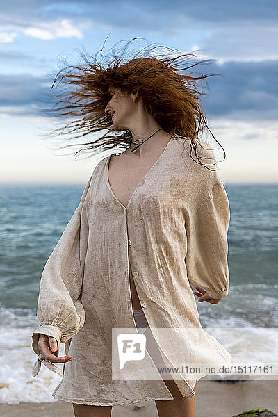 Rothaarige junge Frau wirft ihr Haar am Strand