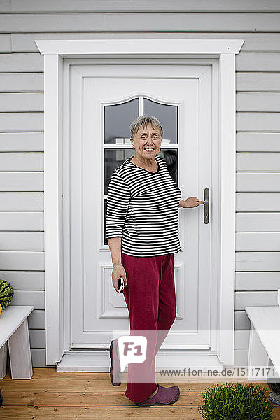 Lächelnde ältere Frau steht auf der Veranda ihres Hauses