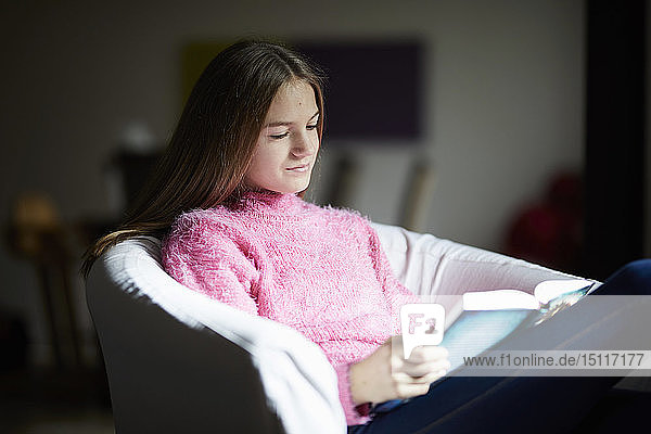 Mädchen sitzt im Sessel und liest ein Buch