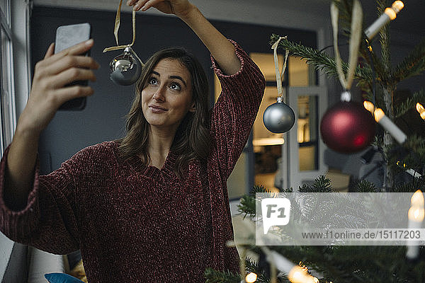 Smiling young woman taking a selfie at Christmas tree