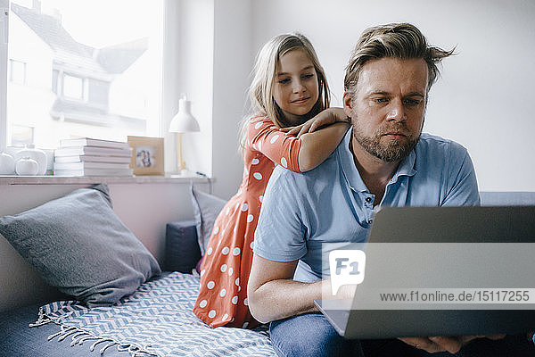 Girl watching father using laptop at home