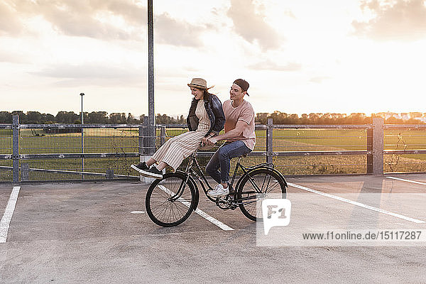 Glückliches junges Paar zusammen auf einem Fahrrad bei Sonnenuntergang auf dem Parkdeck