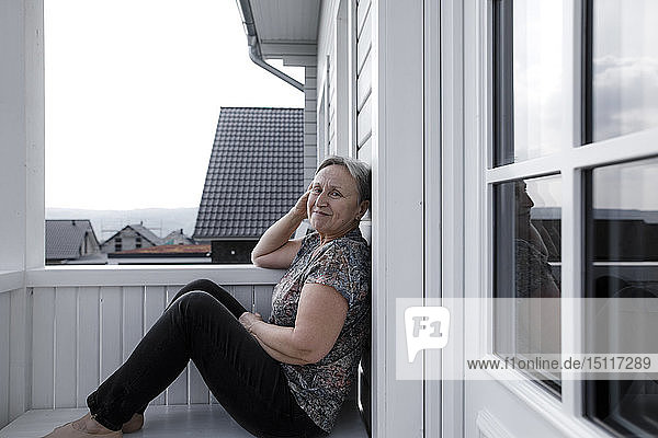 Porträt einer lächelnden  entspannten älteren Frau  die auf der Veranda sitzt