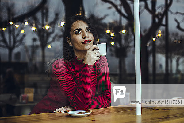 Young woman with cup of coffee behind windowpane in a cafe