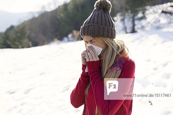 Young blond woman blowing nose in winter
